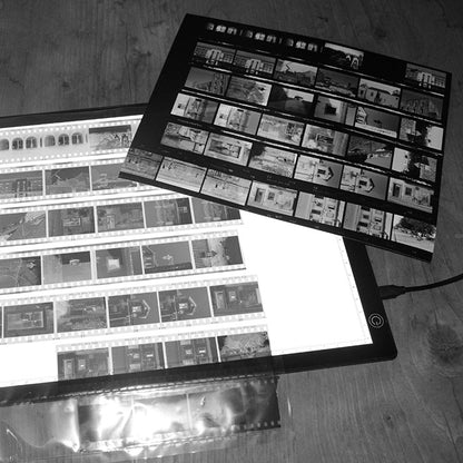 Film strips and a digital tablet displaying film negative images on a wooden surface.